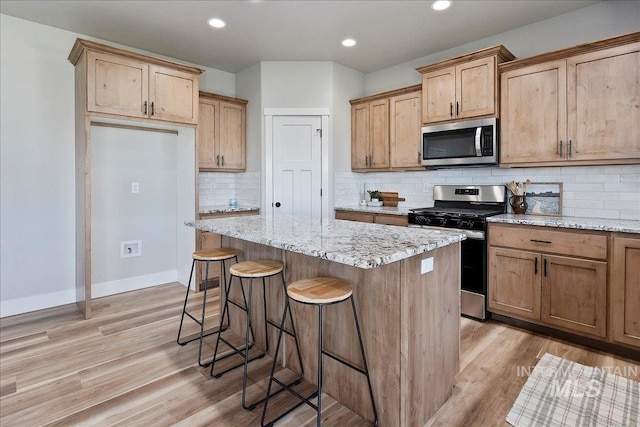 kitchen with a kitchen breakfast bar, tasteful backsplash, appliances with stainless steel finishes, a center island, and light stone countertops