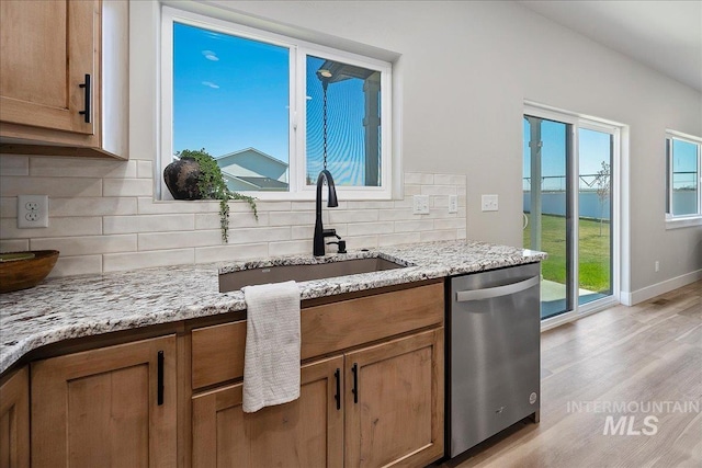 kitchen featuring decorative backsplash, brown cabinets, dishwasher, light wood finished floors, and a sink