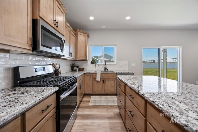 kitchen with light stone countertops, stainless steel appliances, decorative backsplash, and light wood-style flooring