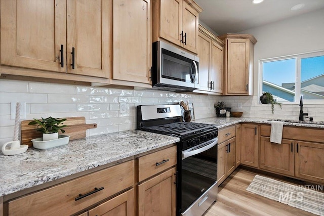 kitchen with light stone countertops, backsplash, appliances with stainless steel finishes, and a sink
