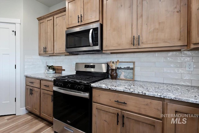 kitchen featuring tasteful backsplash, light stone countertops, appliances with stainless steel finishes, and light wood finished floors