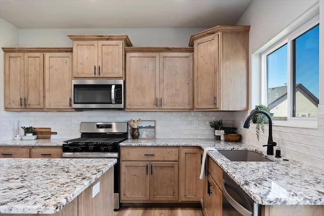 kitchen featuring backsplash, a sink, light stone counters, and appliances with stainless steel finishes