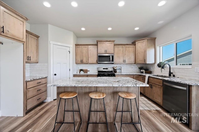 kitchen with tasteful backsplash, wood finished floors, stainless steel appliances, a kitchen bar, and a sink