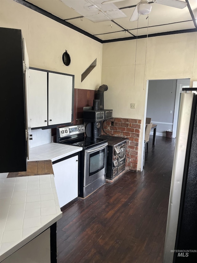 kitchen featuring stainless steel appliances, a ceiling fan, a wood stove, dark wood-style floors, and white cabinetry