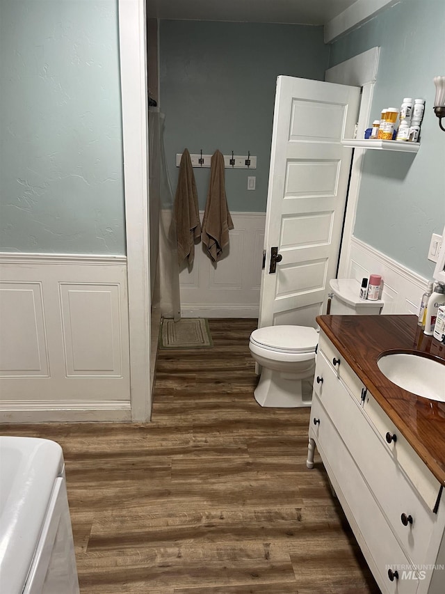 bathroom with wainscoting, wood finished floors, toilet, vanity, and a decorative wall