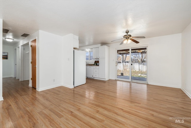 unfurnished living room featuring visible vents, a ceiling fan, light wood-type flooring, and baseboards