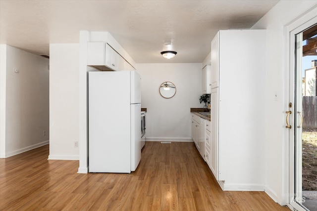 kitchen with white cabinets, baseboards, freestanding refrigerator, and light wood-style floors