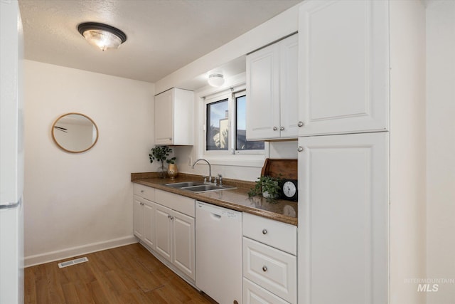 kitchen featuring visible vents, light wood-type flooring, a sink, dark countertops, and white appliances