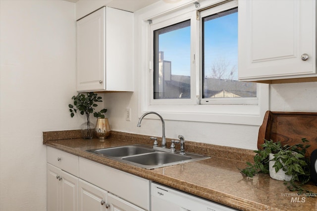 kitchen with dishwasher, dark countertops, white cabinets, and a sink