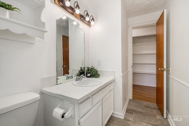 bathroom featuring vanity, toilet, and a wainscoted wall