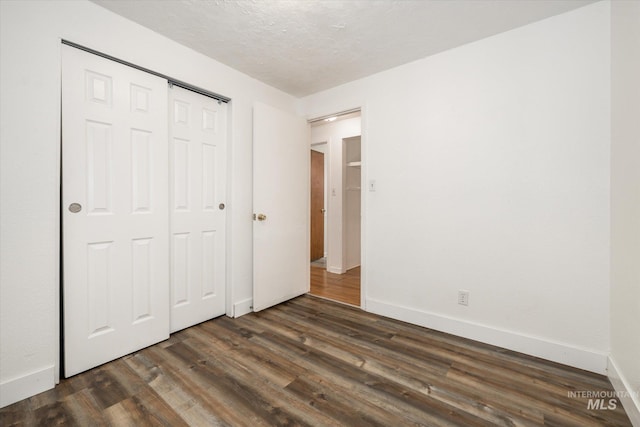 unfurnished bedroom featuring a closet, baseboards, a textured ceiling, and dark wood-style flooring