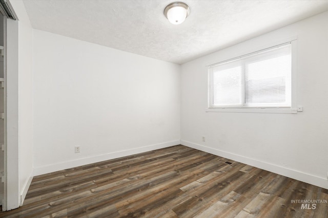 spare room with visible vents, baseboards, a textured ceiling, and dark wood-style floors