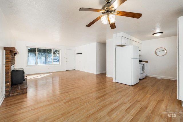 unfurnished living room featuring a ceiling fan, baseboards, a wood stove, light wood-style floors, and a textured ceiling