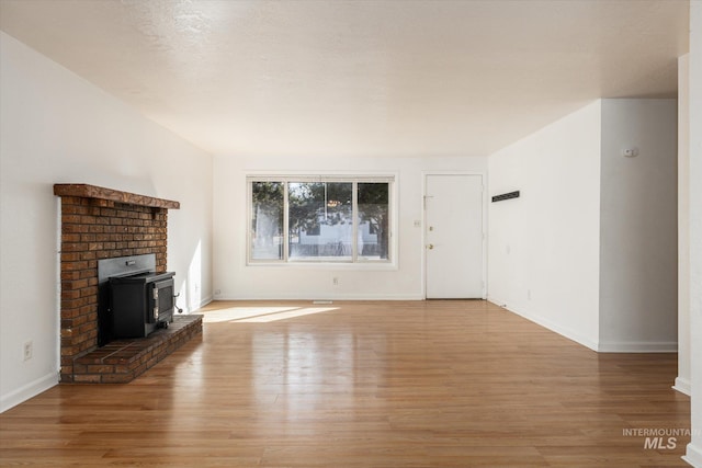 unfurnished living room featuring a wood stove, baseboards, and light wood-type flooring