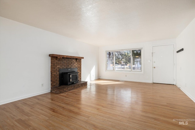 unfurnished living room with baseboards, light wood-style floors, a wood stove, and a textured ceiling