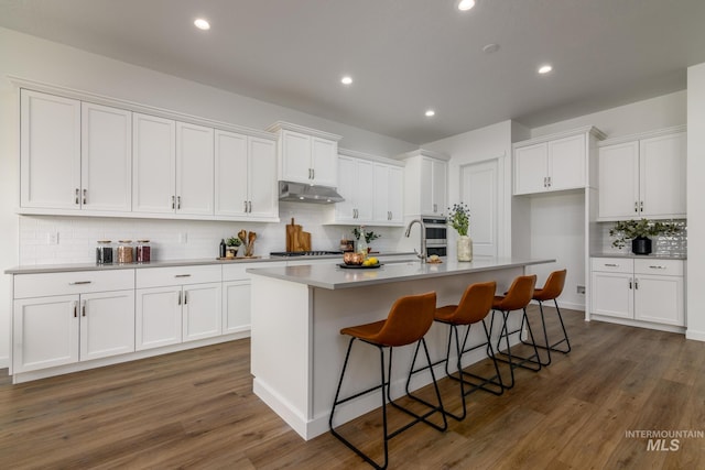 kitchen featuring under cabinet range hood, a center island with sink, and white cabinets