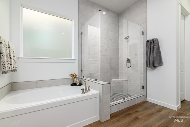 bathroom with a stall shower, wood finished floors, a bath, and baseboards