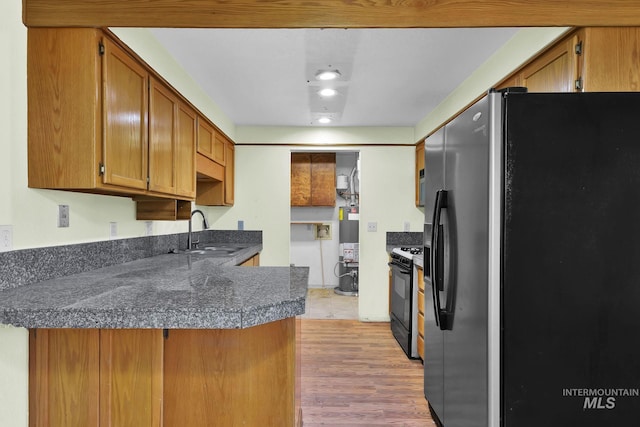 kitchen with sink, gas water heater, black appliances, kitchen peninsula, and light wood-type flooring