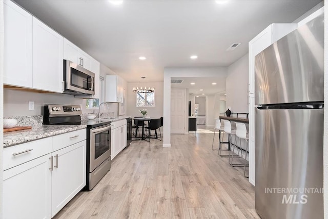 kitchen with a sink, light wood-style floors, stainless steel appliances, white cabinetry, and a notable chandelier