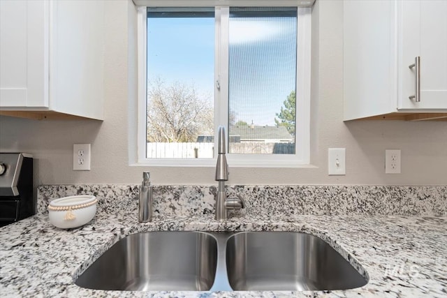 interior details with white cabinets, light stone counters, and a sink