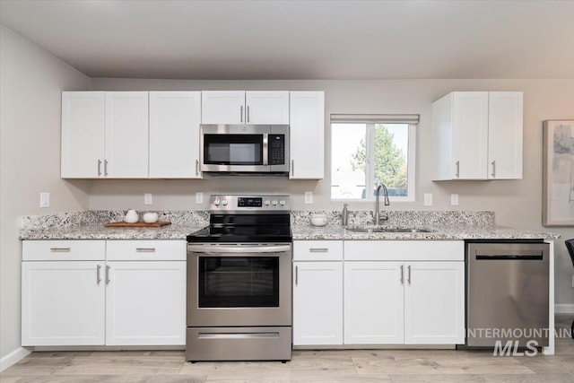 kitchen with white cabinets, light stone counters, a sink, light wood-style flooring, and appliances with stainless steel finishes