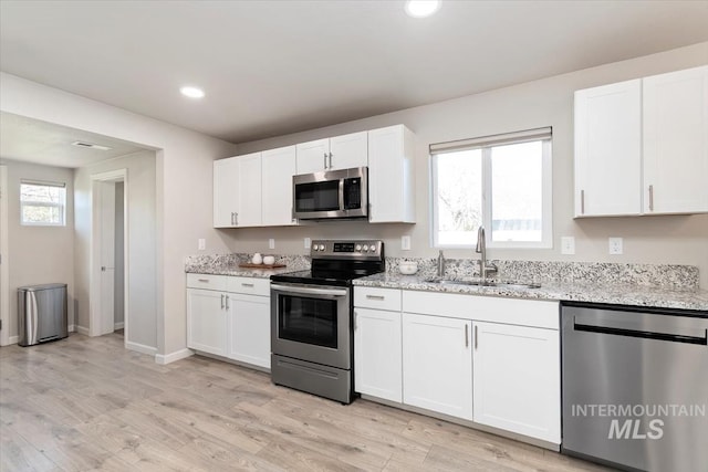 kitchen with light wood finished floors, light stone counters, a sink, appliances with stainless steel finishes, and white cabinetry
