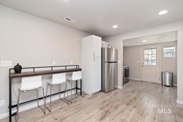 kitchen featuring light wood-style floors, white cabinets, baseboards, visible vents, and freestanding refrigerator