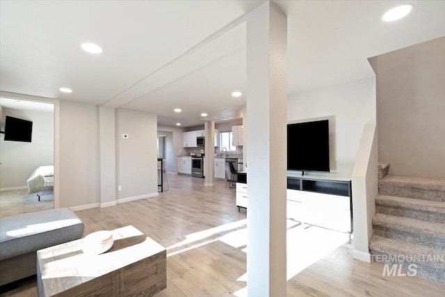living area with recessed lighting, light wood-style floors, baseboards, and stairs