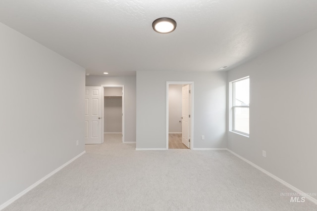 unfurnished bedroom with light carpet, a spacious closet, baseboards, and a closet