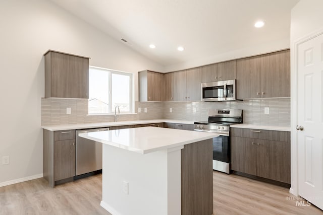 kitchen with light countertops, appliances with stainless steel finishes, light wood-style floors, vaulted ceiling, and a kitchen island