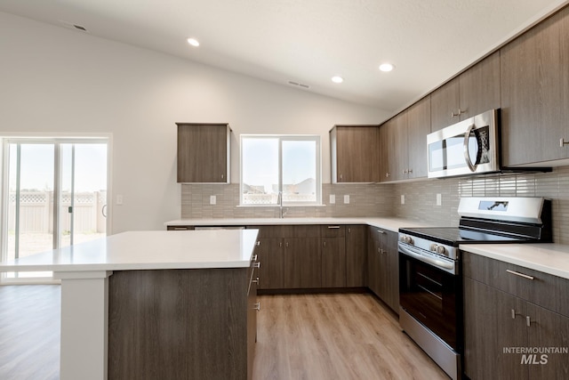 kitchen featuring tasteful backsplash, stainless steel appliances, vaulted ceiling, a center island, and light hardwood / wood-style floors