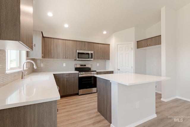 kitchen with stainless steel appliances, light wood finished floors, backsplash, and a sink