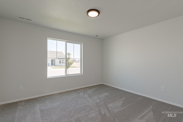 empty room featuring baseboards, visible vents, and dark carpet