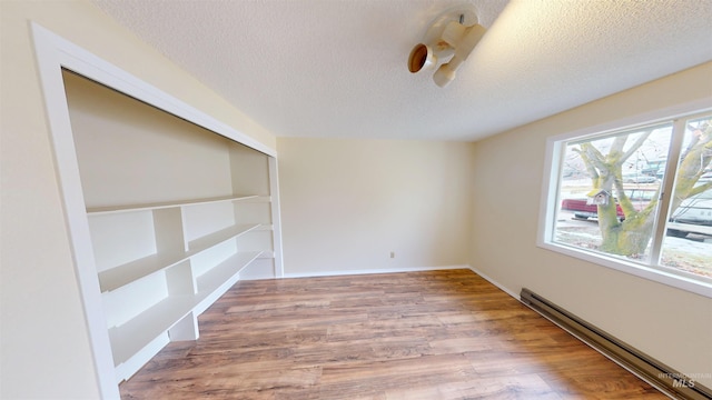 unfurnished room featuring baseboard heating, a textured ceiling, and hardwood / wood-style flooring