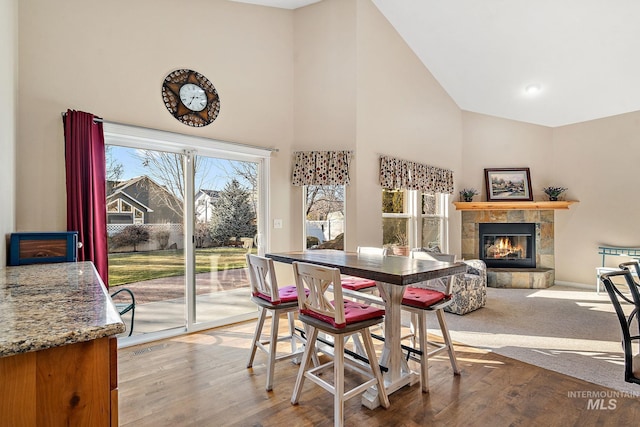 dining area with high vaulted ceiling, a tile fireplace, and wood-type flooring