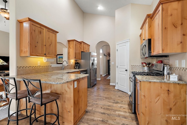 kitchen featuring kitchen peninsula, stainless steel appliances, light hardwood / wood-style floors, a towering ceiling, and sink