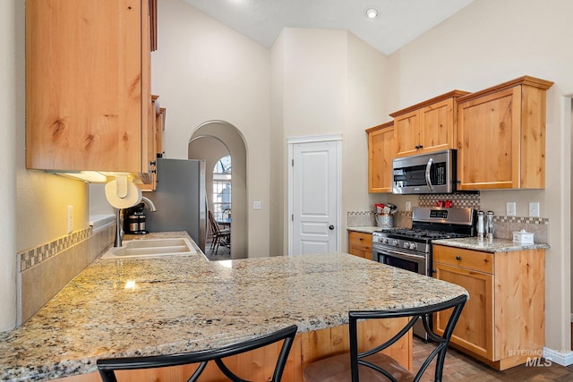 kitchen with stainless steel appliances, sink, light stone counters, kitchen peninsula, and backsplash