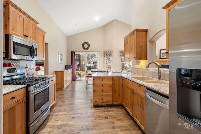 kitchen with stainless steel appliances, sink, light stone counters, light wood-type flooring, and kitchen peninsula