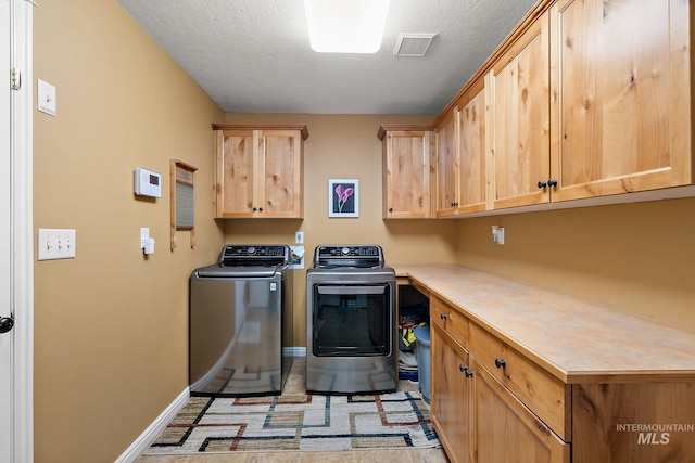 laundry area featuring washer and clothes dryer, a textured ceiling, and cabinets