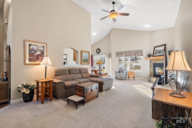 living room with high vaulted ceiling, a tiled fireplace, light carpet, and ceiling fan