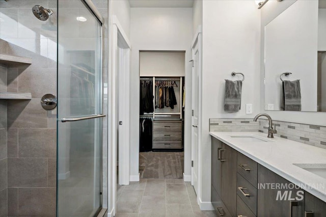 full bath featuring a spacious closet, a stall shower, backsplash, and a sink