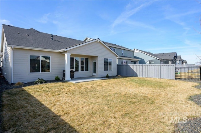 rear view of property featuring a yard, a patio area, a shingled roof, and fence