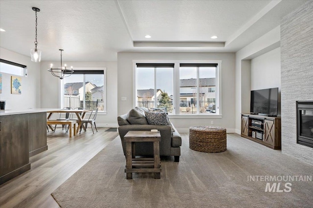 living area featuring a notable chandelier, light wood-style floors, baseboards, and a textured ceiling