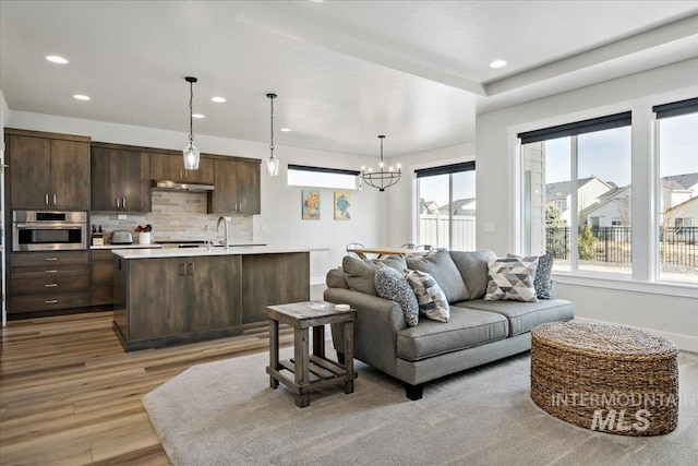 living room with a notable chandelier, recessed lighting, baseboards, and light wood-type flooring