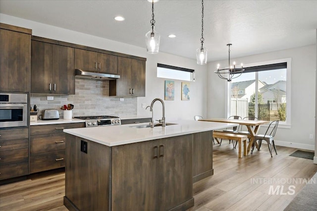 kitchen featuring a sink, under cabinet range hood, light countertops, stainless steel oven, and range