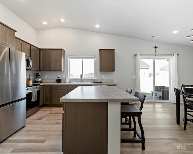 kitchen with a center island, lofted ceiling, a wealth of natural light, appliances with stainless steel finishes, and a kitchen breakfast bar