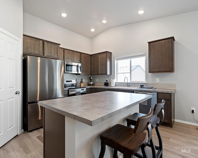 kitchen featuring stainless steel appliances, dark brown cabinets, light wood-type flooring, and a kitchen breakfast bar