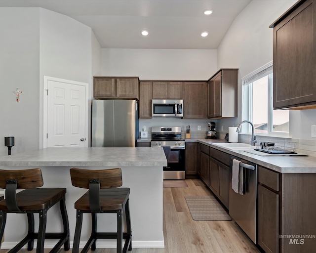 kitchen featuring appliances with stainless steel finishes, a breakfast bar, dark brown cabinets, light wood-type flooring, and a sink