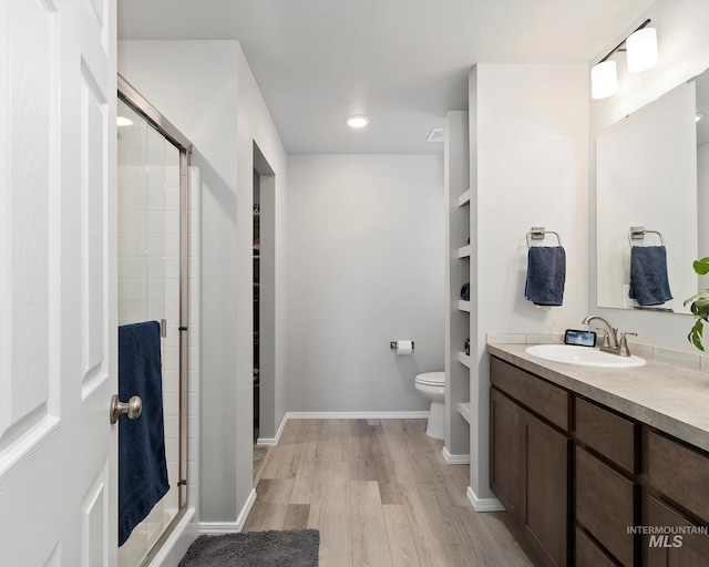 full bath featuring toilet, vanity, a shower stall, wood finished floors, and baseboards