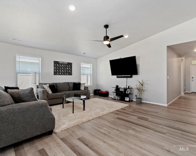 living room featuring lofted ceiling, visible vents, light wood-style floors, a ceiling fan, and baseboards